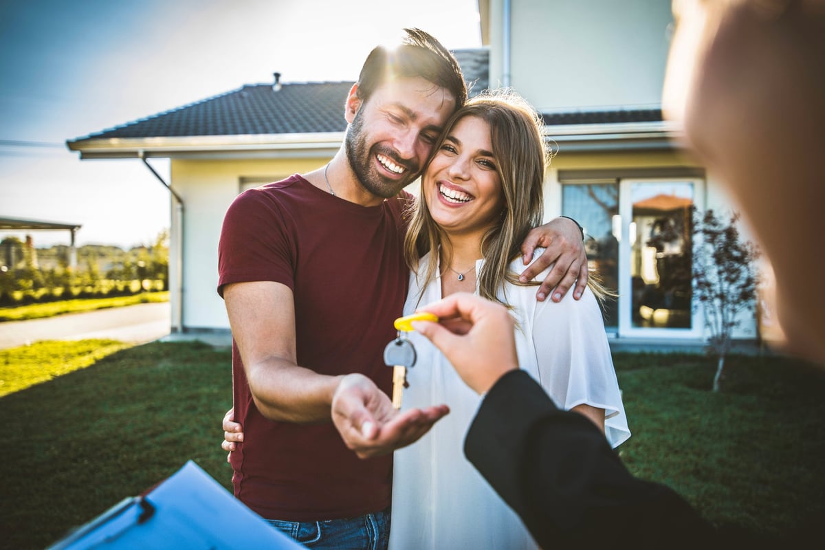 Happy millennial couple receiving keys from real estate agent purchasing real estate