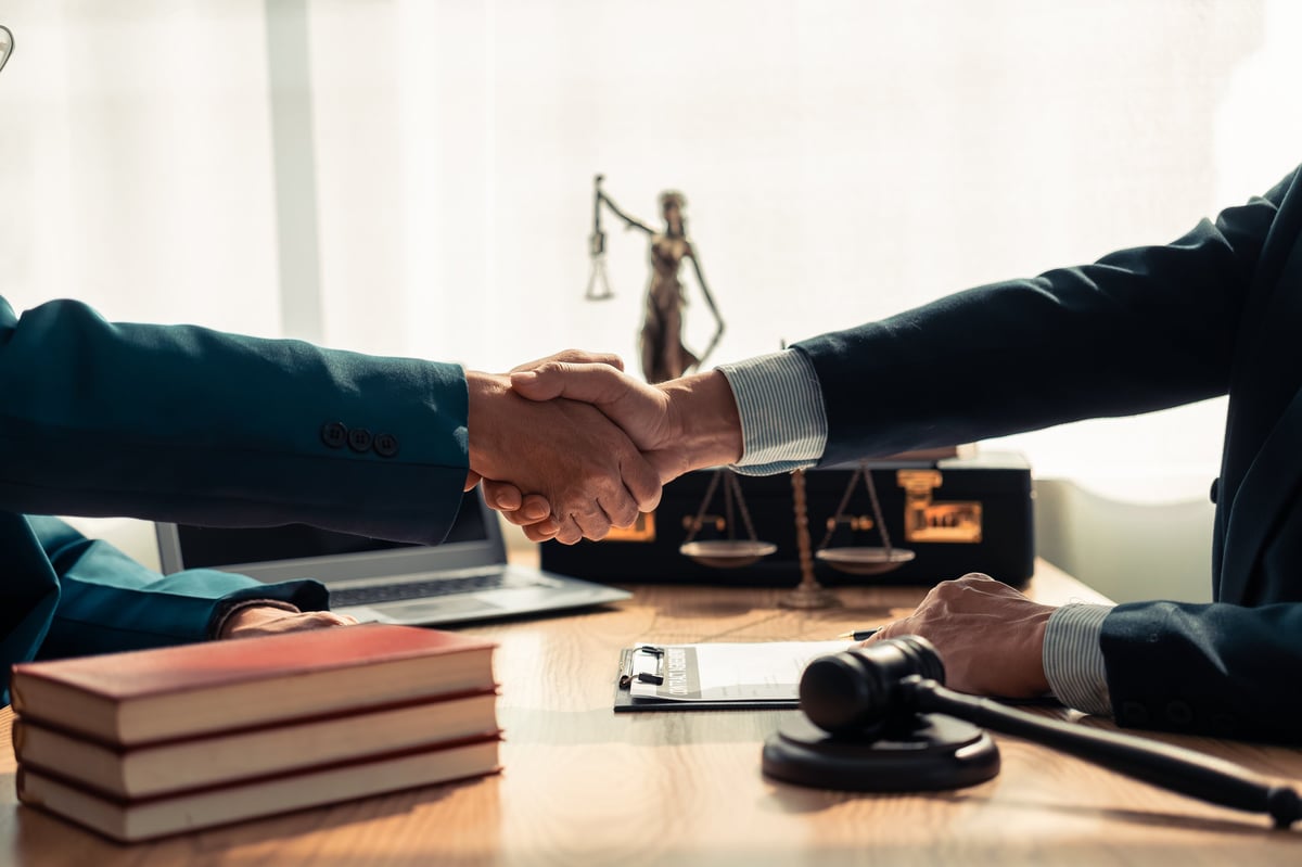 Close-up of lawyer and client shaking hands on table symbolizing trust in a legal contract with a hammer and statue representing justice