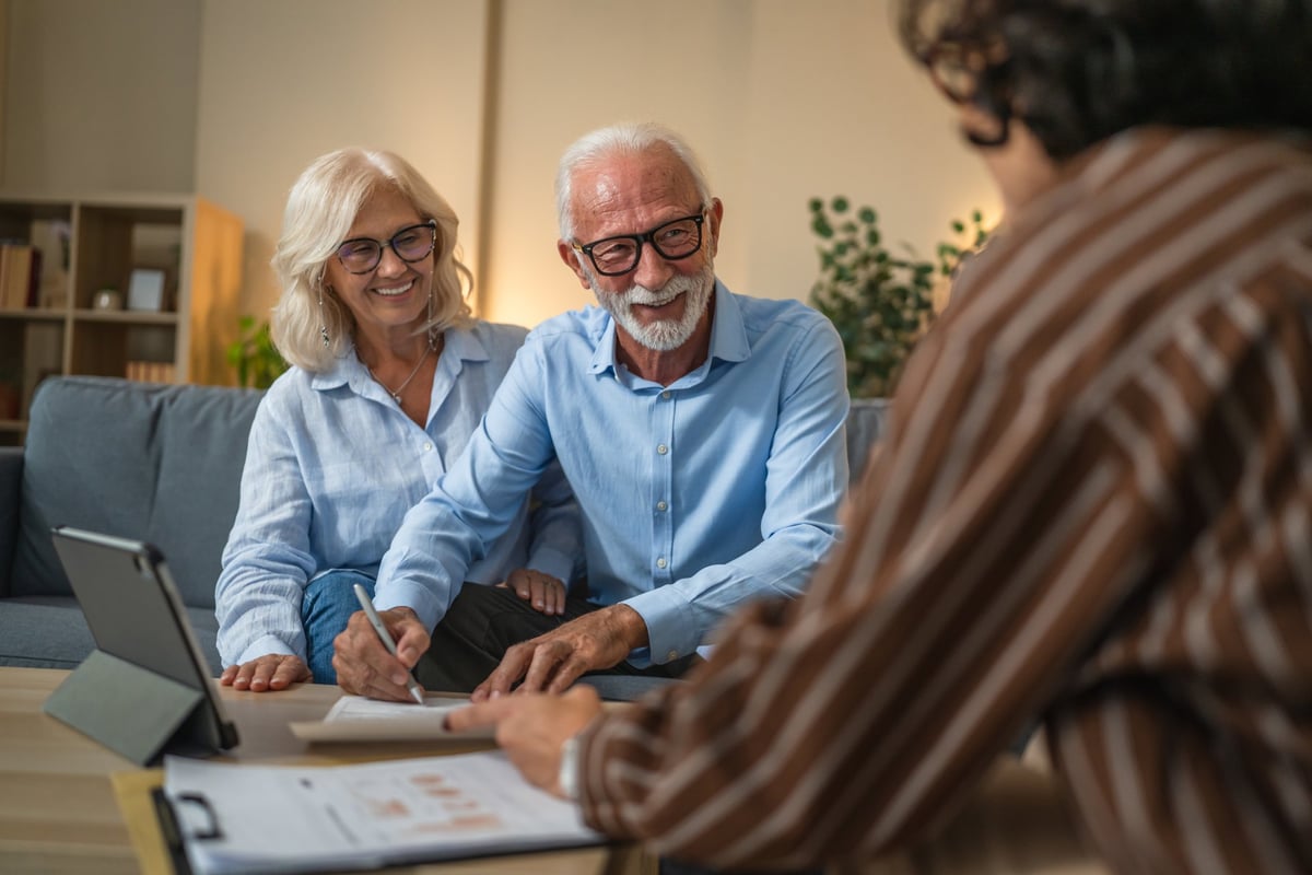 Senior couple signing an insurance policy contract with a woman financial adviser at home