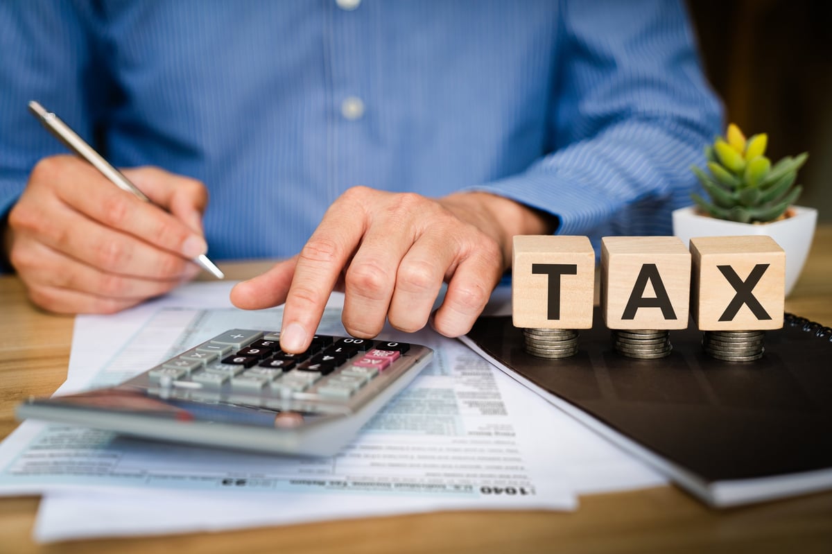 Business professional calculating tax with calculator and pen on financial documents with wooden TAX blocks