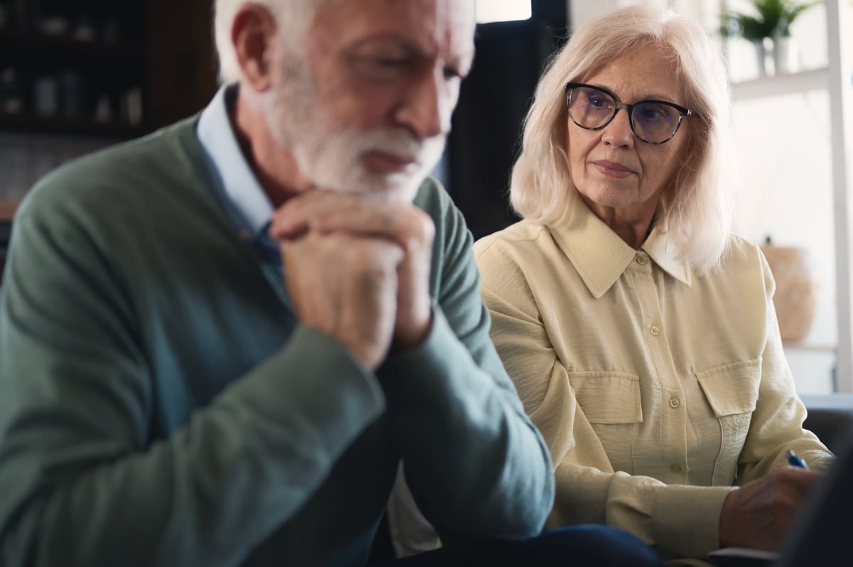 Stressed senior couple reviewing bills and finances at home, using laptop and paperwork. Worried about rising costs, retirement savings, and household expenses in uncertain times