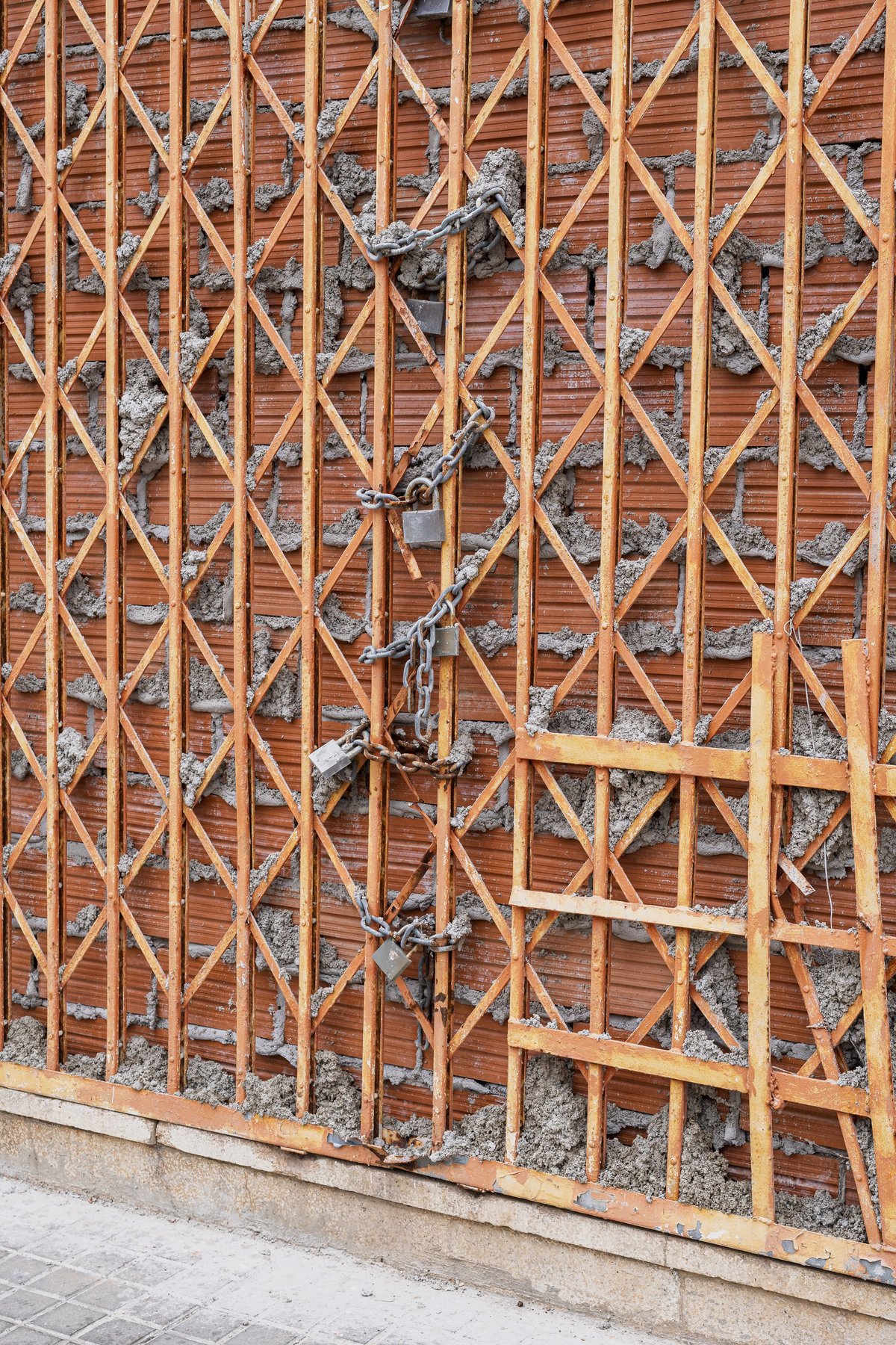 A rusty metal gate firmly locked with chains and padlocks over a bricked entrance