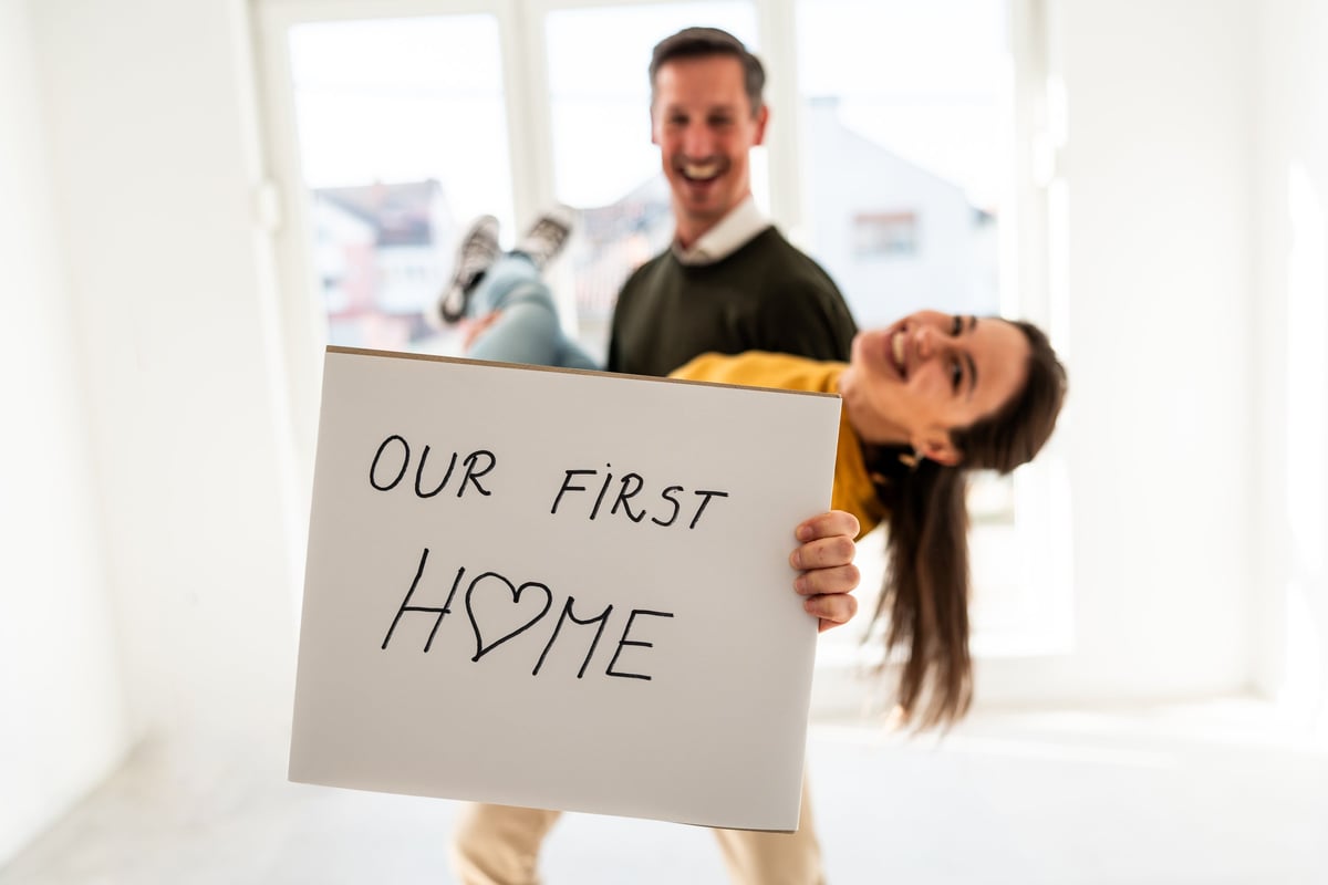 Joyful young couple celebrating moving into their first home holding a sign reading our first home