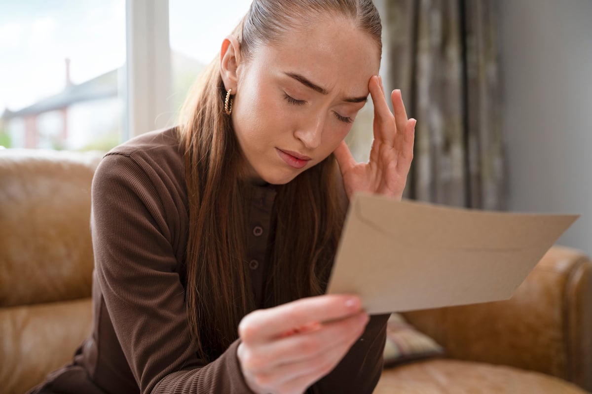 A woman looks at a piece of paper with a concerned look while sitting on a brown sofa